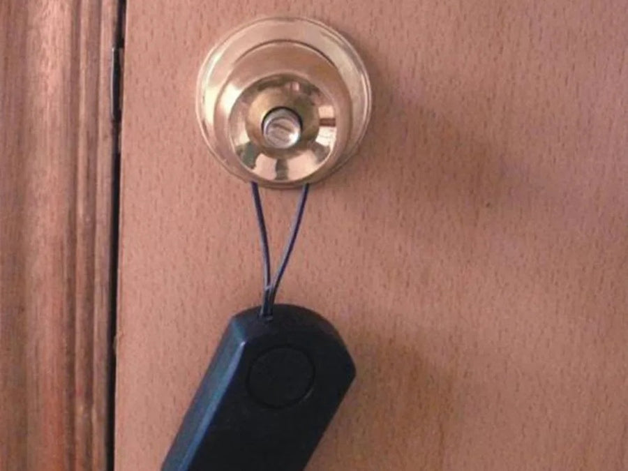 Small black touch alarm hanging by a cord from a brass knob on an apartment door