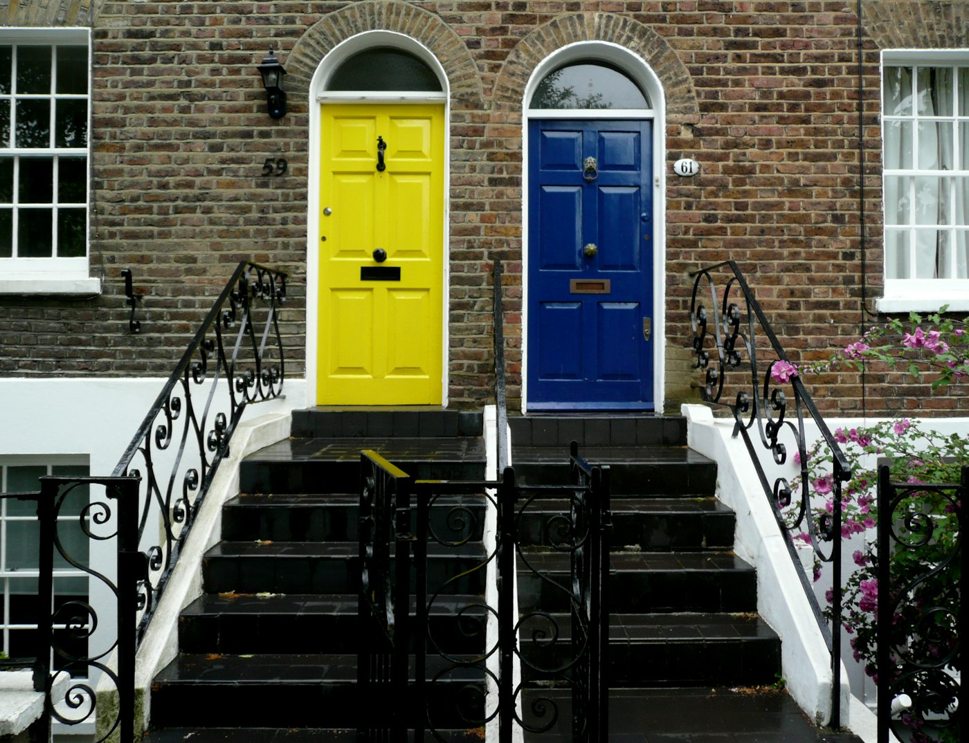 Two apartment doors, yellow and blue, on a brick townhouse with front steps
