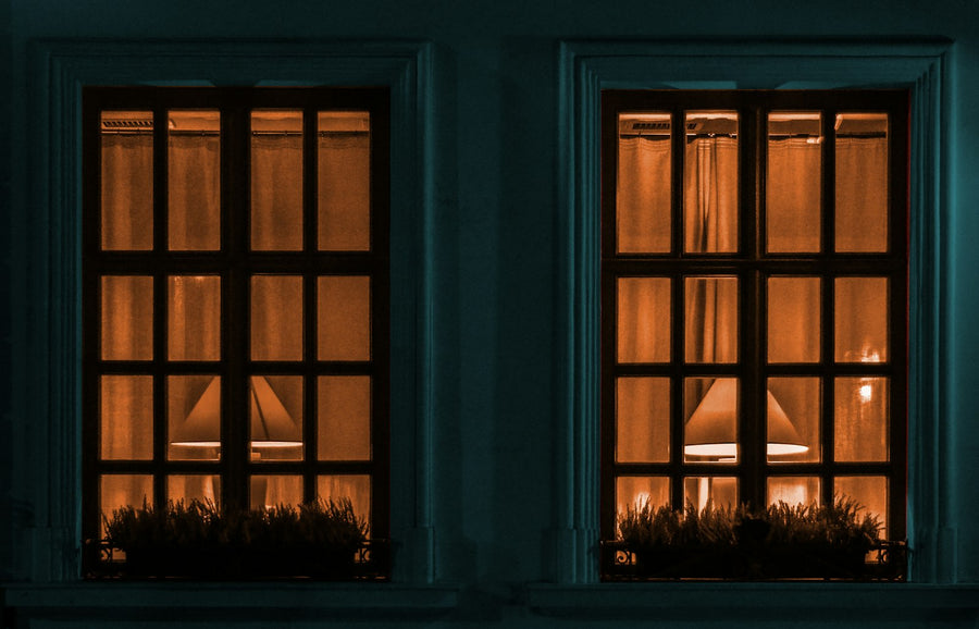 Two windows of a home glowing warmly at night, seen from the street