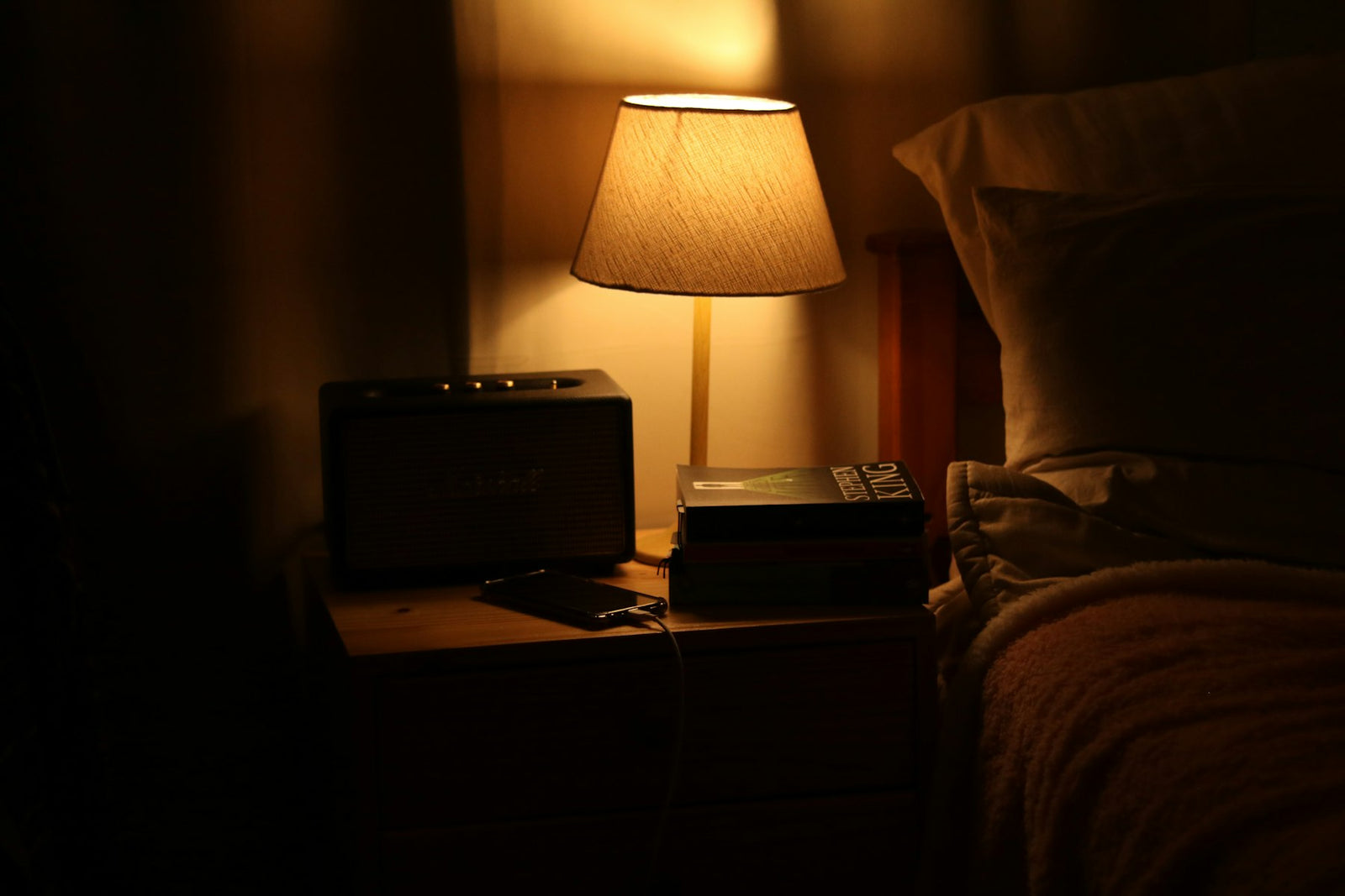 Bedside lamp glowing over a nightstand with a small radio