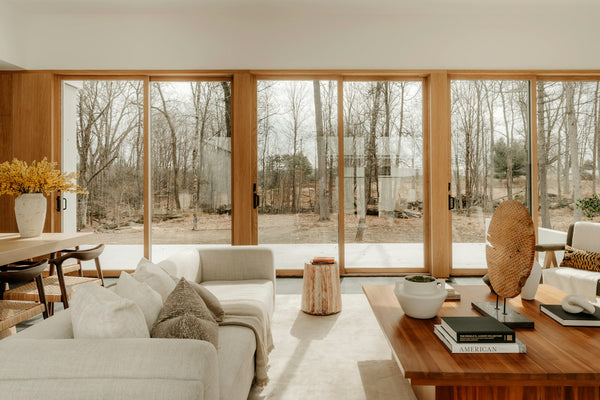 A calm living room with a wall of wood-framed sliding glass patio doors opening onto a deck and bare winter trees.