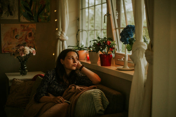 Woman relaxing on a couch beside a bright open window with plants