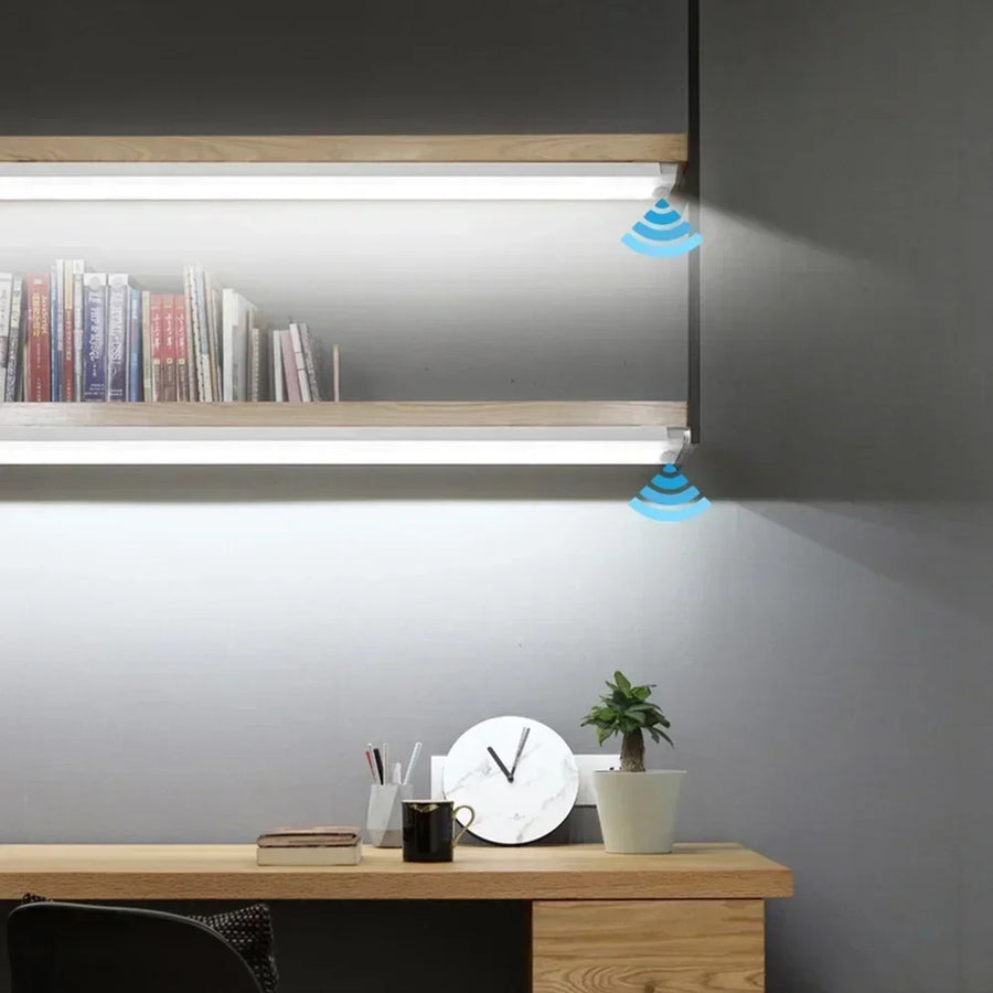 Slim LED motion sensor light bars lit under two wooden shelves above a desk