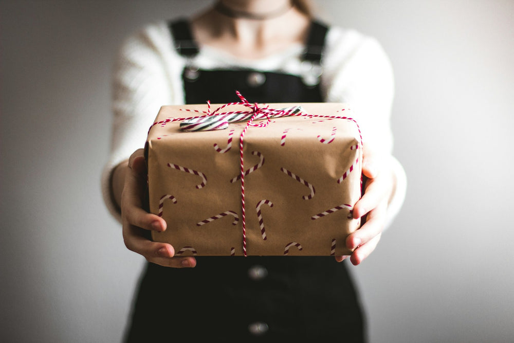 A person holding out a gift wrapped in brown paper with red and white string