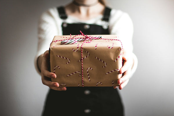 A person holding out a gift wrapped in brown paper with red and white string