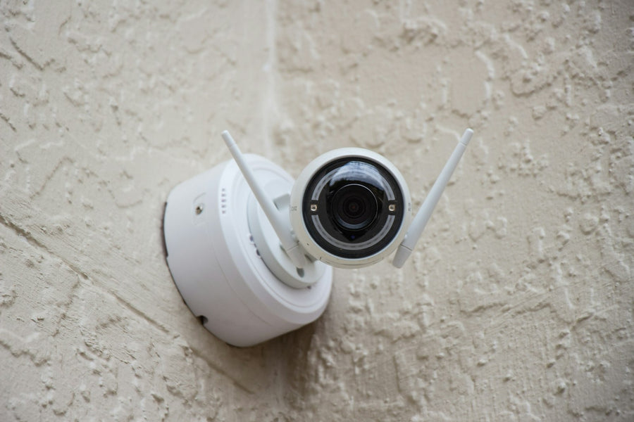 Small white wireless security camera mounted on the light exterior wall of a home