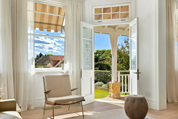 White French doors with leaded glass panels swung open outward onto a sunny porch, a garden and hedge beyond.
