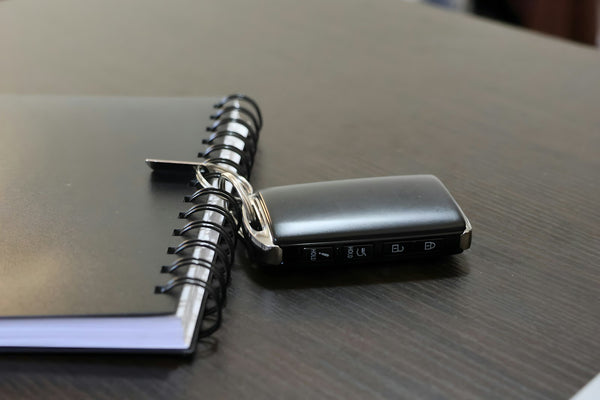 A keyless car smart key fob lying on a dark wooden table beside a spiral notebook