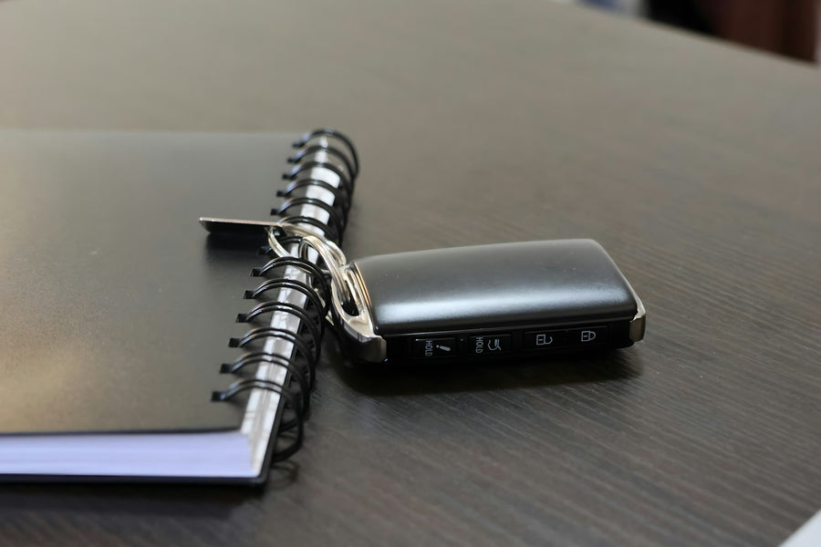 A keyless car smart key fob lying on a dark wooden table beside a spiral notebook