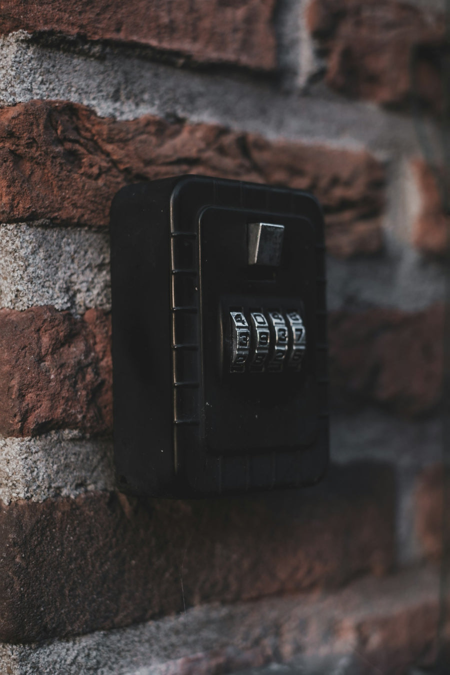 A black four-dial combination lock box mounted on a red brick wall, dials showing.