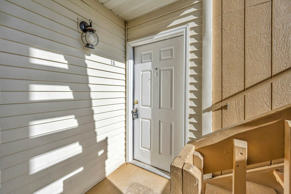 White six-panel front door with a deadbolt above the knob, in a sunlit entry with light siding