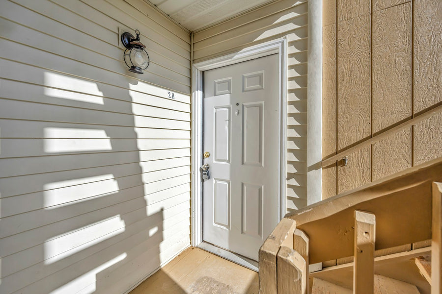 White six-panel front door with a deadbolt above the knob, in a sunlit entry with light siding