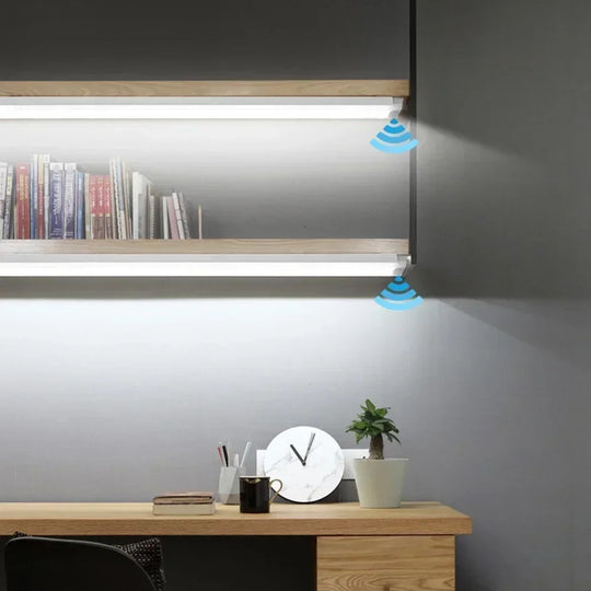 Slim LED motion sensor light bars lit under two wooden shelves above a desk