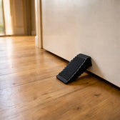 Black ribbed rubber door wedge pushed under a closed white interior door on a light wood floor