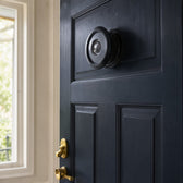 Black 220° door viewer fitted at eye height in a dark navy front door, seen from inside
