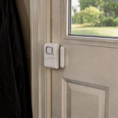 White door entry alarm stuck on a back door frame, its magnet piece on the door right beside it