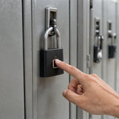 A finger on the sensor of a black fingerprint padlock locking a grey metal gym locker