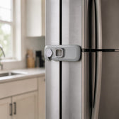 Grey adhesive refrigerator lock fixed across the door gap of a stainless steel fridge in a bright kitchen