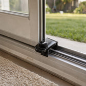 Black no-drill lock clamped on the bottom track of a white sliding patio door, holding it open a few inches