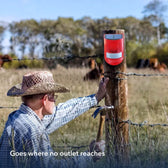 Man hanging the red solar siren on a wooden fence post at the edge of a pasture