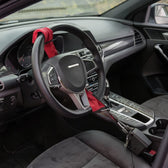 Red padded steering wheel lock looped around a car steering wheel and clipped into the seat-belt buckle
