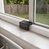 Black window sash lock clamped on the bottom track of a white kitchen sliding window, butted against the closed pane